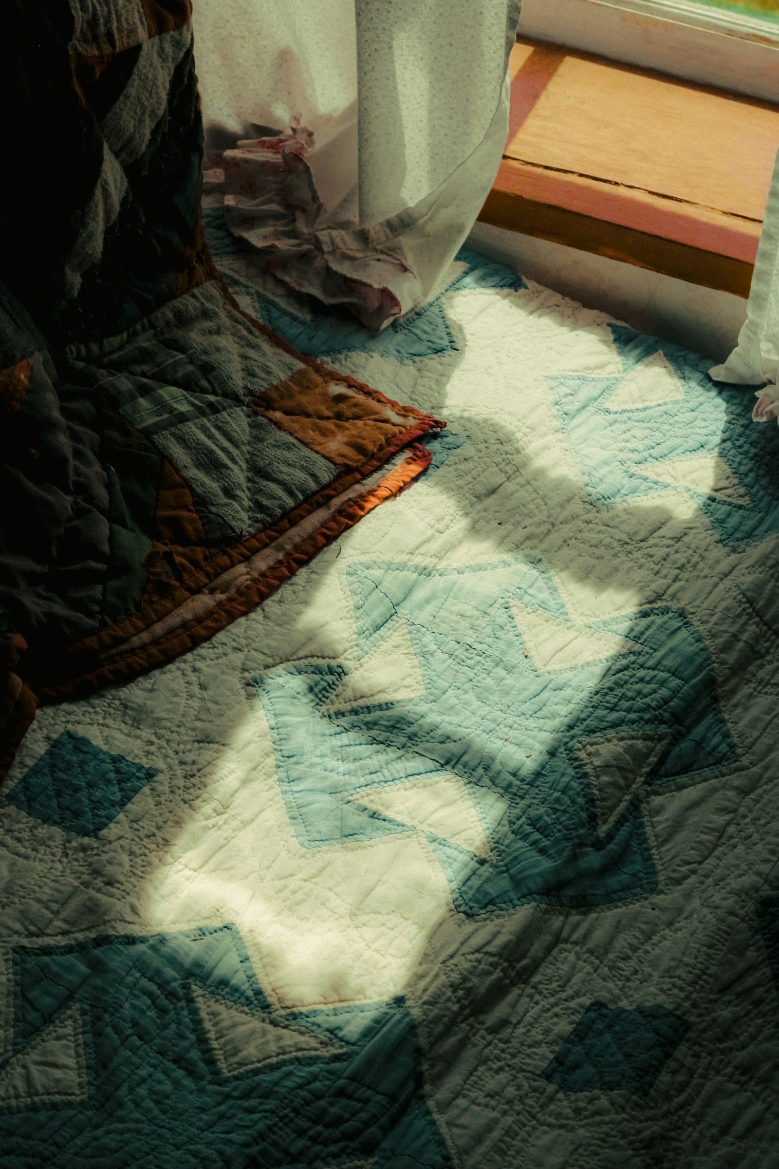 A quilted bed beside a window in gentle morning light