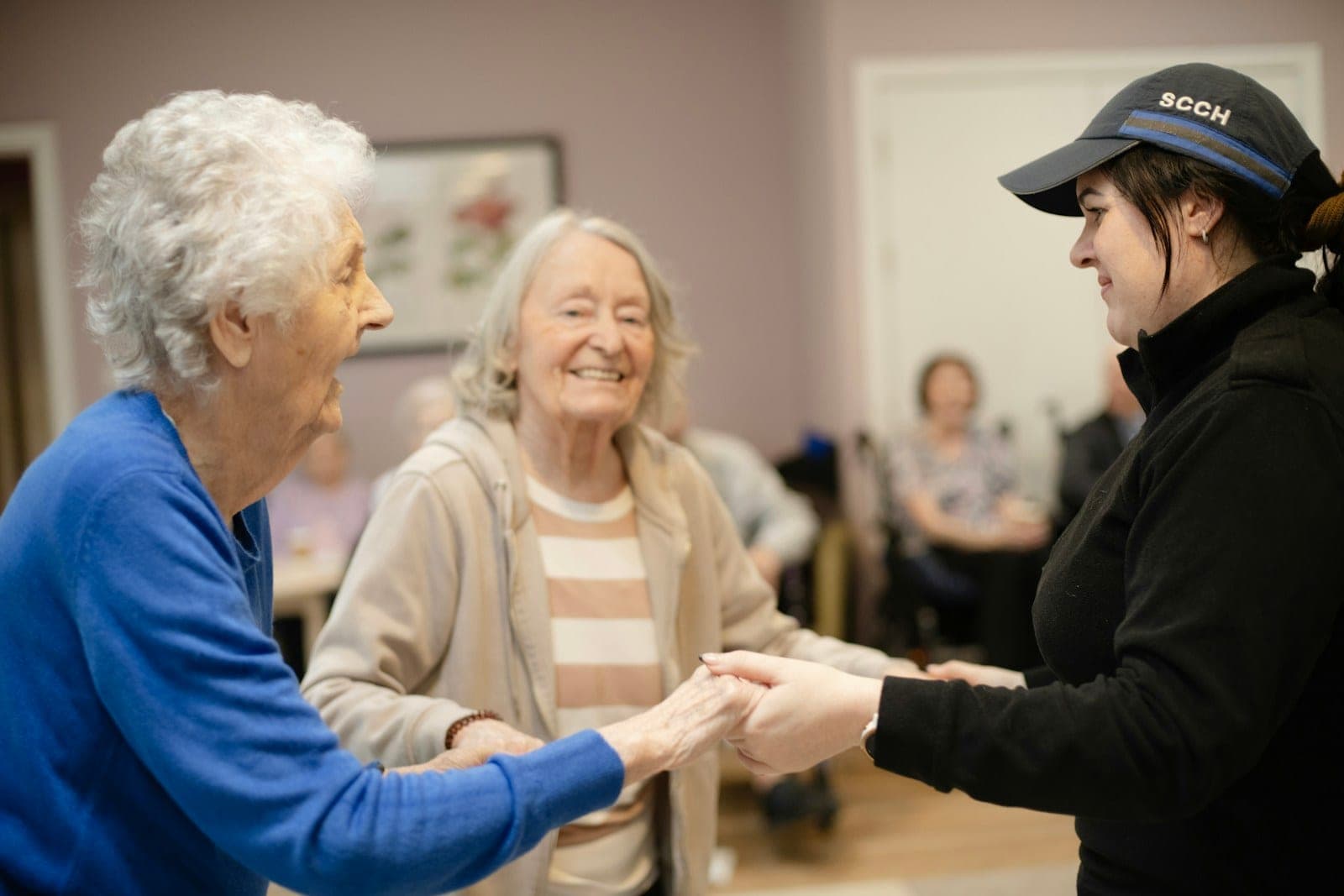 A caregiver holding hands with two older women during a visit