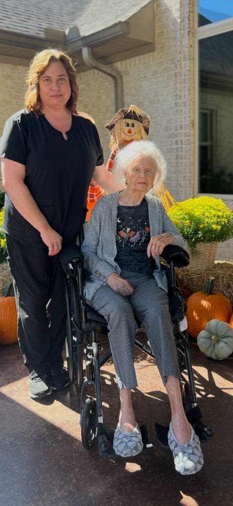 Beth standing beside Betty Jean Lee Smith in a wheelchair, in front of the pumpkins